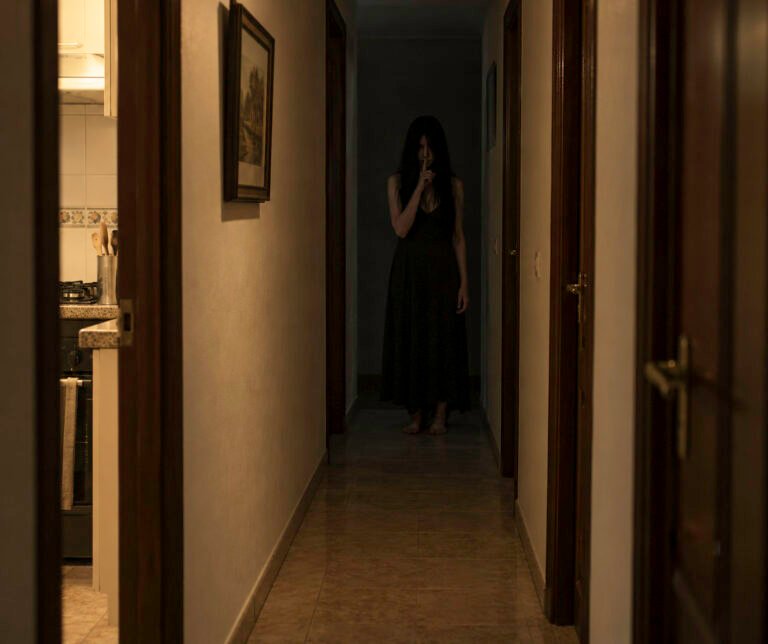 Pasillo de una vivienda con poca luz y una silueta oscura al fondo